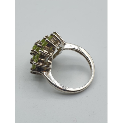 285 - Stone set silver and peridot ring. Mounted on a silver band and having 19 stones in a flower formati... 