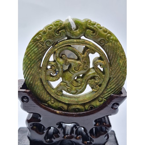 46 - A Chinese carved green jade disc (amulet?) with mythical beasts on a custom made wooden base. Disc d... 