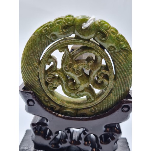 46 - A Chinese carved green jade disc (amulet?) with mythical beasts on a custom made wooden base. Disc d... 