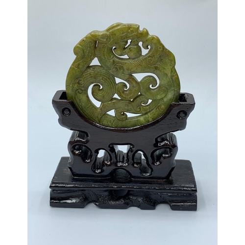 20 - A Chinese carved green jade disc (amulet?) with a dragon and stylistic representations of clouds and... 