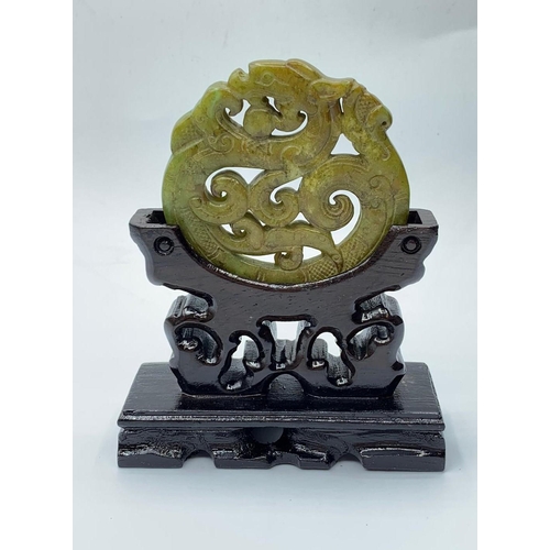 20 - A Chinese carved green jade disc (amulet?) with a dragon and stylistic representations of clouds and... 