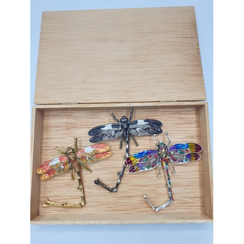 92 - Three large dragonfly brooches in a wooden box. Enamel applied by hand on various metals with imitat... 