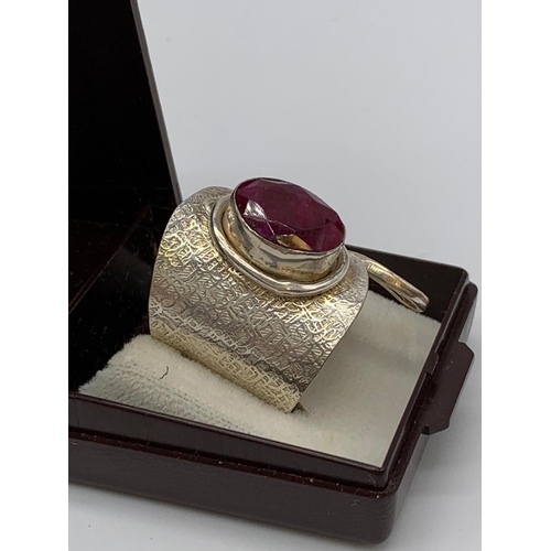 126 - An unusual artisan’s silver (stamped 925) ring with a big faceted oval ruby      
central stone in i... 