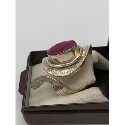 126 - An unusual artisan’s silver (stamped 925) ring with a big faceted oval ruby      
central stone in i... 