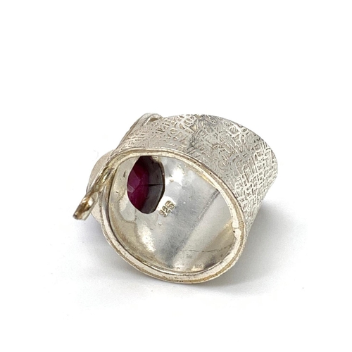 126 - An unusual artisan’s silver (stamped 925) ring with a big faceted oval ruby      
central stone in i... 