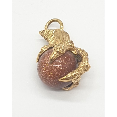 523 - Yellow metal charm/pendant of a claw clutching a ball, weight 3.9g