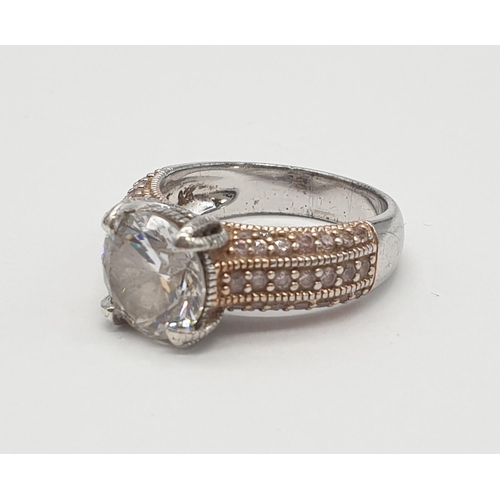 476 - Silver ring having rose coloured shoulders encrusted with gems and a large faceted clear stone in fo... 