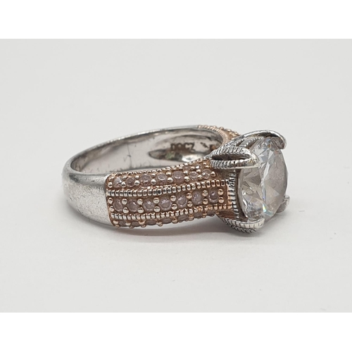 476 - Silver ring having rose coloured shoulders encrusted with gems and a large faceted clear stone in fo... 