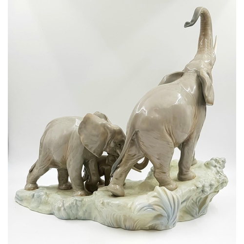 69 - This spectacular Lladro porcelain piece depicts a family of elephants ascending a rock-led by a trum... 