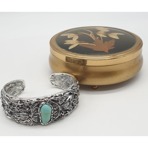 126 - A white metal (untested) and turquoise bangle. Presented in a vintage brass round case with dried fl... 