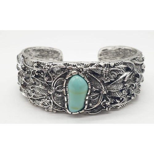 126 - A white metal (untested) and turquoise bangle. Presented in a vintage brass round case with dried fl... 