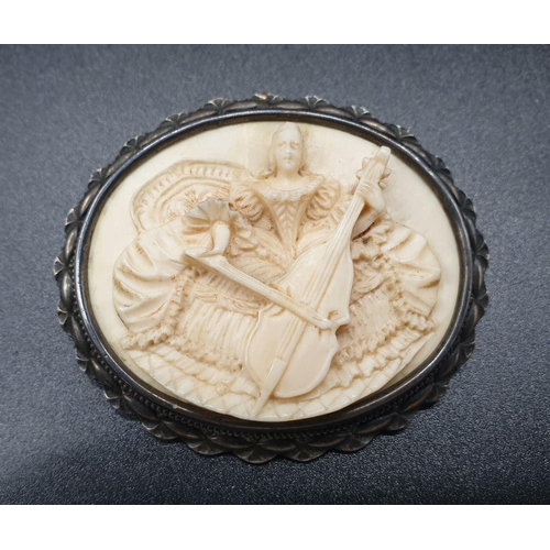 195 - An antique hand-carved ivory brooch on silver base - depicting a lady playing a cello. 20.5g total w... 