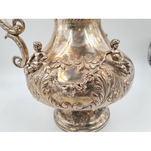82 - A LARGE SPANISH SILVER ETRUSCAN SHAPED WATER JUG, HAND DECORATED WITH CHERUBS AND FLORA.
1.2kg and 3... 