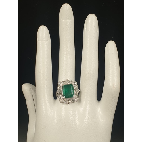 340 - AN 18CT WHITE GOLD RING SET WITH A LARGE EMERALD CUT NATURAL EMERERALD CENTRE STONE AND 16 ROSE CUT ... 