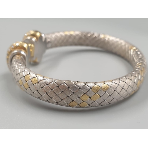 564 - AN OVAL 18CT YELLOW AND WHITE GOLD BANGLE WITH DIAMOND ENCRUSTING. 31.5gms.