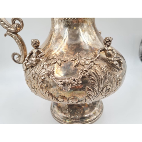 157 - A LARGE SPANISH SILVER ETRUSCAN SHAPED WATER JUG, HAND DECORATED WITH CHERUBS AND FLORA.
1.2kg and 3... 