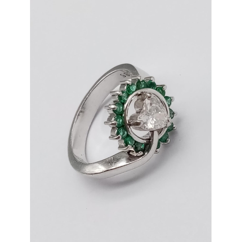 110 - A PLATINUM RING CONTAINING A HEART SHAPED CENTRAL DIAMOND SURROUNDED BY EMERALDS.
6.8gms     SIZE K/... 