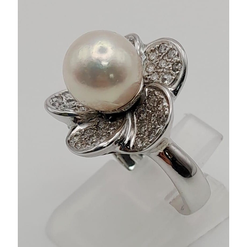 60 - An attractive 18 K white gold ring with a diamond studded flower on top and a genuine round white pe... 