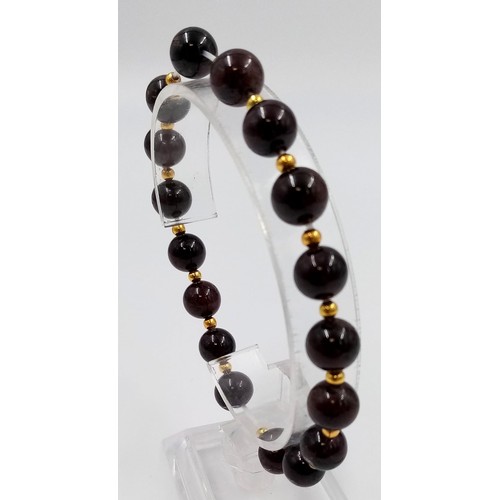 886 - An Expandable Garnet Bead Bracelet with Gilded Spacers.