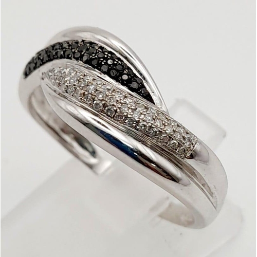 559 - An 18K White Gold Diamond Crossover Ring. White and black diamonds. Size S. 3.2g total weight.