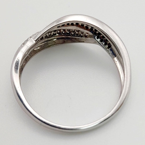 559 - An 18K White Gold Diamond Crossover Ring. White and black diamonds. Size S. 3.2g total weight.