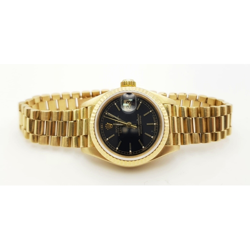 667 - An 18 k yellow gold, ladies, ROLEX DATEJUST watch. 26 mm dial, black face with gold hands and hour m... 