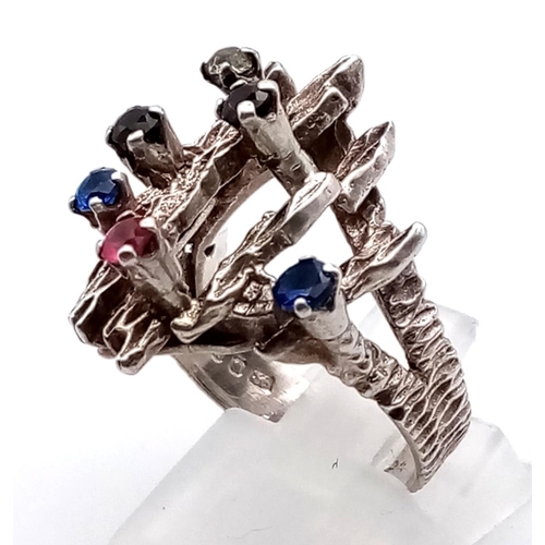 1105 - A SILVER FASHION RING ENHANCED WITH GEMSTONES.  7.7gms  size O