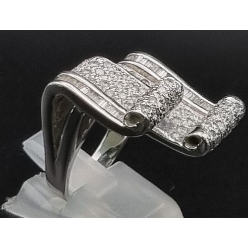 88 - An 18 K white gold ring with two scrolls loaded with baguette and brilliant cut diamonds. Ring size:... 