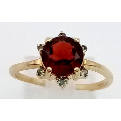 421 - A 9K Yellow Gold Red and Green Garnet Ring. Large central red garnet with a halo of small green garn... 