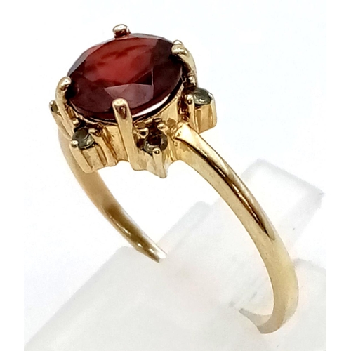 421 - A 9K Yellow Gold Red and Green Garnet Ring. Large central red garnet with a halo of small green garn... 