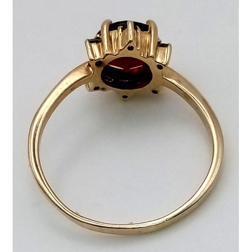 421 - A 9K Yellow Gold Red and Green Garnet Ring. Large central red garnet with a halo of small green garn... 