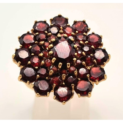 167 - 9K YELLOW GOLD GARNET CLUSTER RING. 7.1G. SIZE L