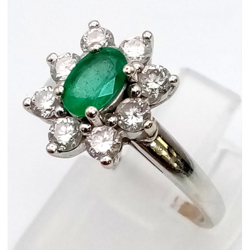 100 - An 18K White Gold Emerald and Diamond Ring. Central oval emerald - 0.5ct surrounded by eight petals ... 