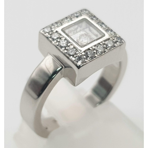 53 - An 18K White Gold Floating Diamond Ring. A square of diamonds shield a central floating diamond. Siz... 