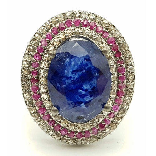 587 - 8.55ct Oval Cut Blue Sapphire ring with a halo of rubies and two rows of 1.25cts diamonds in a pave ... 