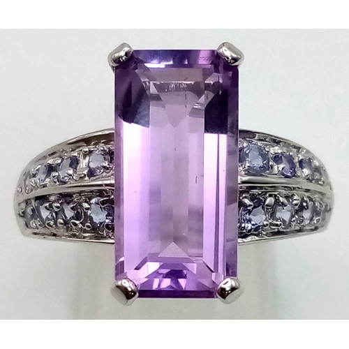 171 - A 9K White Gold Amethyst and Tanzanite Ring. Large clean central baguette-cut amethyst with eight ro... 