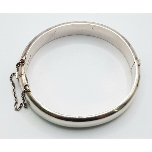 530 - A sterling silver hinged bangle with safety chain. Inner diameter 58 mm, weight: 21.3 g.