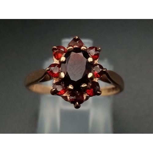 669 - A Vintage 9K Yellow Gold Garnet Ring. Central garnet oval stone surrounded by a halo of smaller garn... 