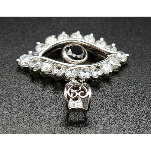 676 - An 18K White Gold Sapphire and Diamond Eye Pendant. Blue sapphire pupil surrounded by an outer eye-s... 