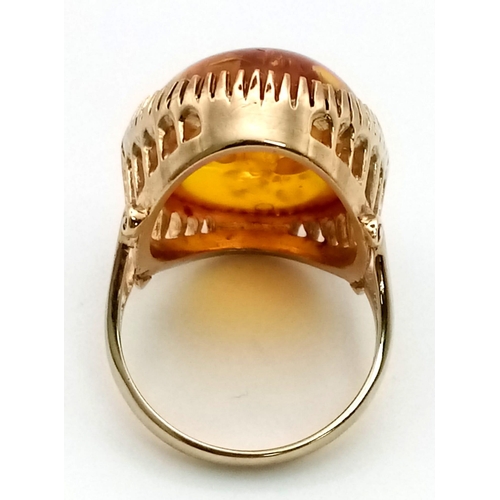 31 - A 9K Yellow Gold Amber Ring. A large natural amber cabochon set in pierced decorative gold. Wonderfu... 