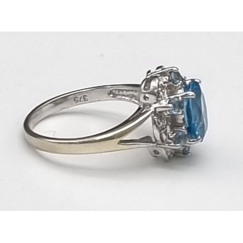 261 - A 9K White Gold Blue Topaz and Diamond Ring. A scene-stealing central blue topaz complimented with s... 