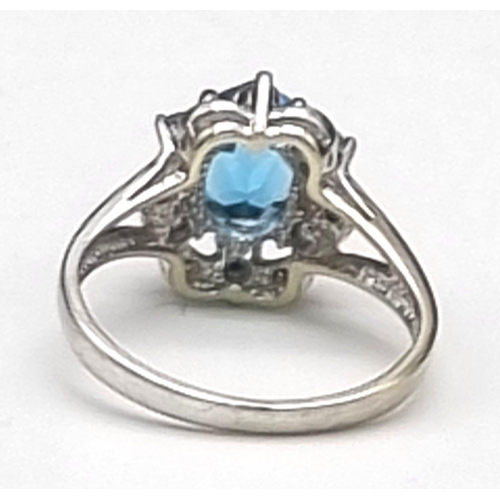 261 - A 9K White Gold Blue Topaz and Diamond Ring. A scene-stealing central blue topaz complimented with s... 