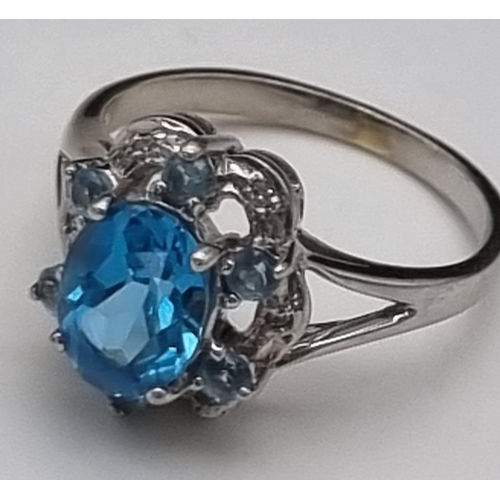 261 - A 9K White Gold Blue Topaz and Diamond Ring. A scene-stealing central blue topaz complimented with s... 