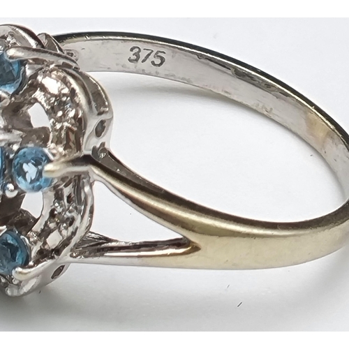 261 - A 9K White Gold Blue Topaz and Diamond Ring. A scene-stealing central blue topaz complimented with s... 