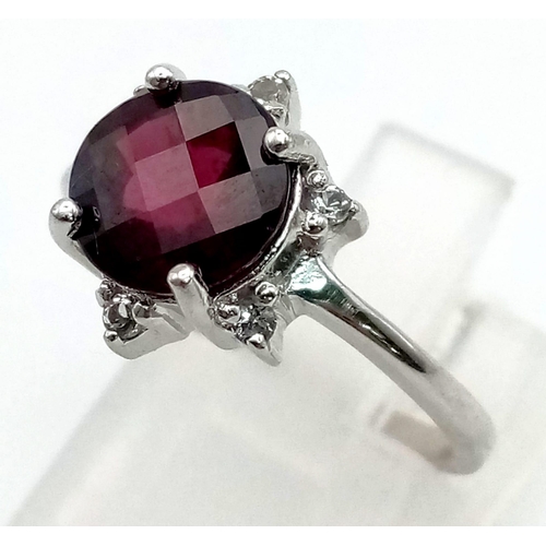 549 - A 9K White Gold Garnet and Diamond Ring. A round-cut, well-faceted central garnet complimented with ... 