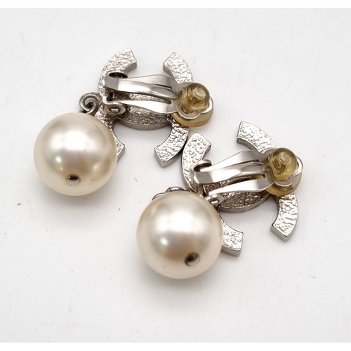 17 - A Pair of Chanel Monogram Pearl Earrings. Comes in a Chanel pouch with box. On white metal. 3cm drop... 