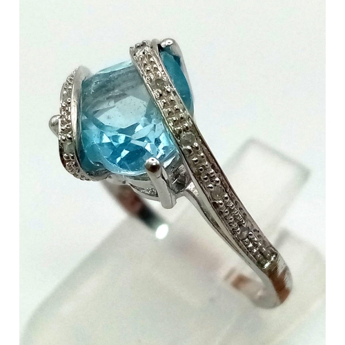 259 - A 9K White Gold Blue Topaz and Diamond Ring. Central blue topaz covered with two waves of diamonds. ... 