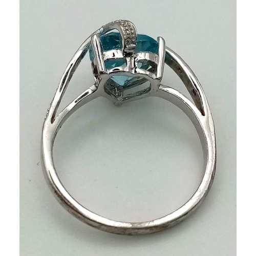 259 - A 9K White Gold Blue Topaz and Diamond Ring. Central blue topaz covered with two waves of diamonds. ... 