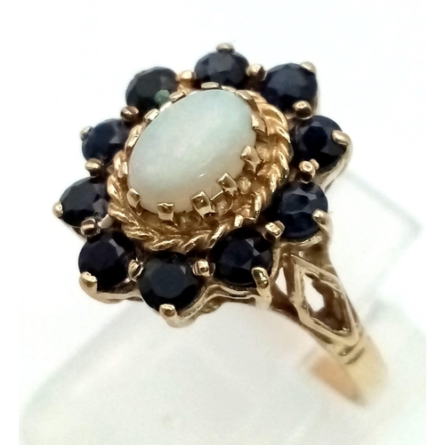 348 - An Edwardian 9K Yellow Gold Sapphire and Opal Ring. Central oval Opal cabochon surrounded by a halo ... 