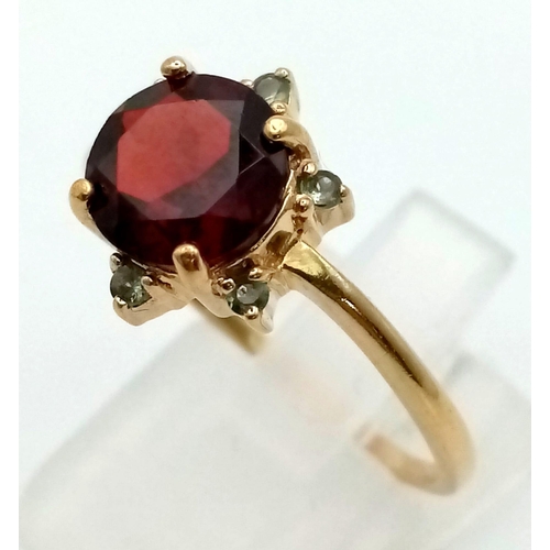 567 - An Antique 9k Yellow Gold Red and Green Garnet Ring. Central blood red garnet with a halo of six sma... 